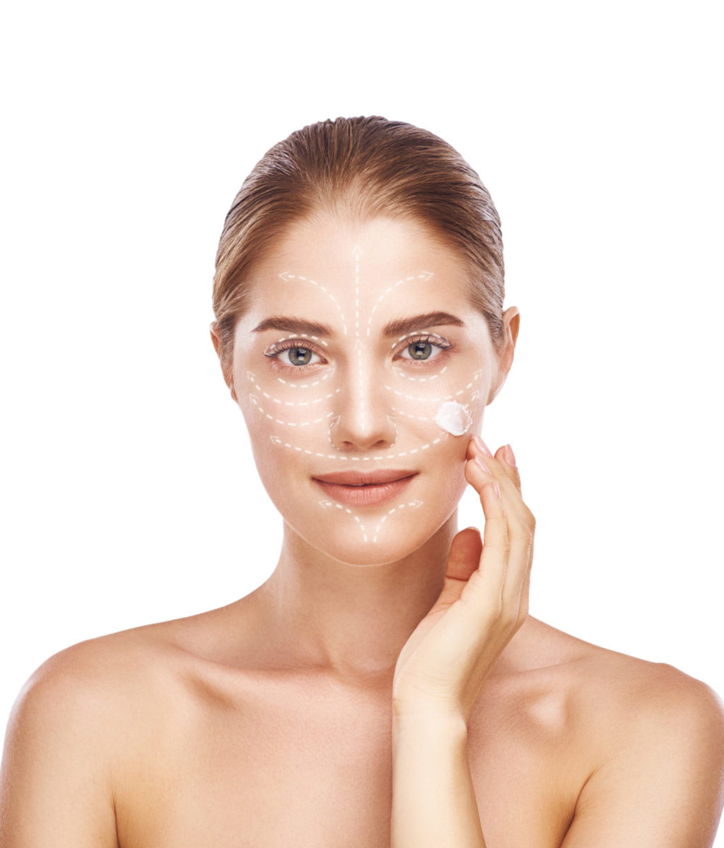The importance of skin cream. Healthy and beautiful woman with graphic arrows over her face testing moisturizer cream while standing against white background. Skin care concept. Cosmetic products